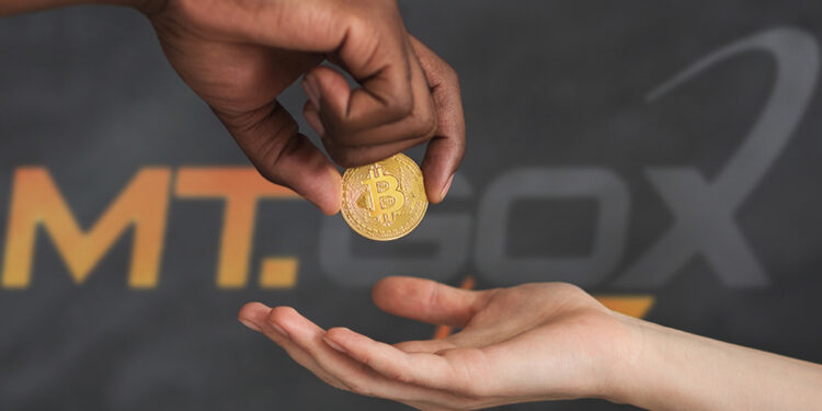persona entregando moneda de bitcoin en mano con logo de MT Gox en le fondo