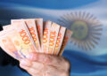 persona sostiene billetes de pesos argentinos con bandera de Argentina en el fondo