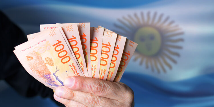 persona sostiene billetes de pesos argentinos con bandera de Argentina en el fondo