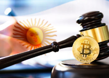 moneda de bitcoin junto a martillo de juez con bandera de Argentina y persona escribiendo ley en el fondo