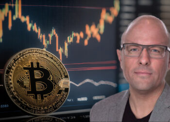 Rian Wilday junto a moneda de bitcoin apoyada en pantalla con grafico de precio ascendiendo