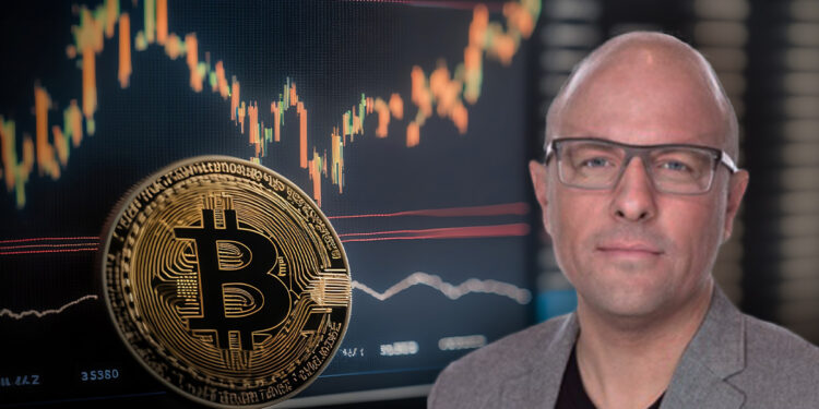 Rian Wilday junto a moneda de bitcoin apoyada en pantalla con grafico de precio ascendiendo