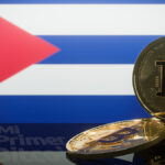 monedas de bitcoin con pantalla proyectando bandera de Cuba en el fondo y logo de Mi primer Bitcoin reflejado en mesa