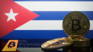 monedas de bitcoin con pantalla proyectando bandera de Cuba en el fondo y logo de Mi primer Bitcoin reflejado en mesa