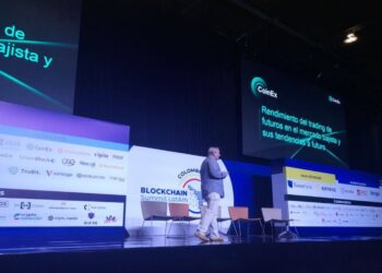 Un hombre de traje camina sobre el escenario de la Blockchain Summit Latam con imagenes de CoinEx detras.