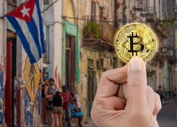 mano sosteniendo moneda de bitcoin con paisaje de Cuba en el fondo