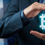 manos sosteniendo logo de bitcoin con edificios de empresa en el fondo