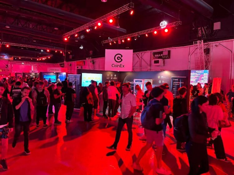 Muchas personas caminando en el pasillo frente al stand de CoinEx.