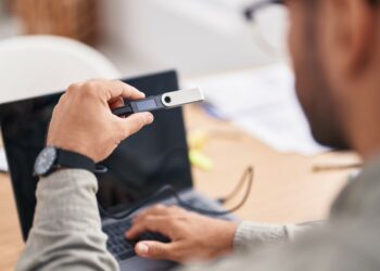 Una persona sostiene una hardware wallet frente a una laptop