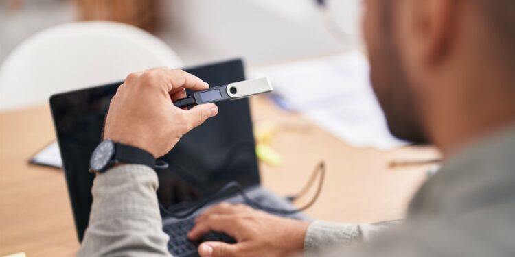 Una persona sostiene una hardware wallet frente a una laptop
