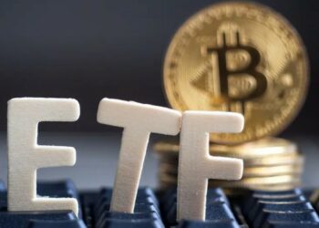 Las siglas ETF sobre un teclado y con una moneda de Bitcoin al fondo