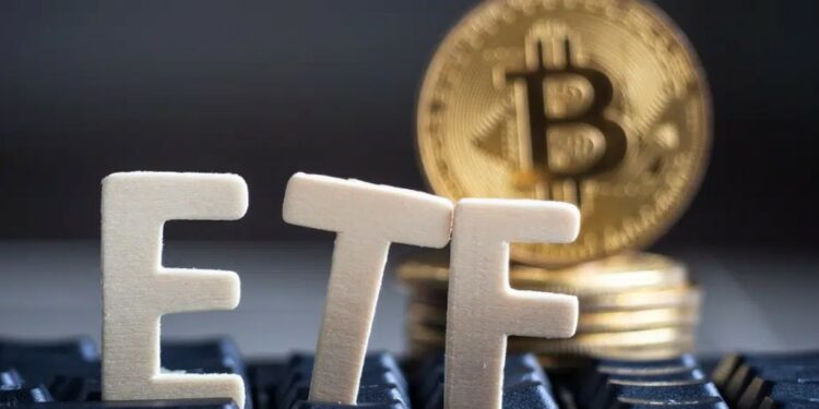 Las siglas ETF sobre un teclado y con una moneda de Bitcoin al fondo