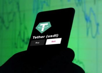 Una mano sostiene un celular y en la pantalla se destaca a Tether.