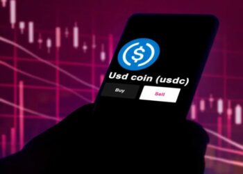 Un teléfono con USDC en la pantalla y gráficos de precio al fondo