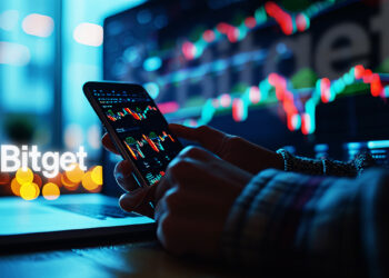 Un teléfono con gráficos de trading y el logo de Bitget al fondo