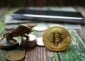 Una moneda física de bitcoin y una escultura de un toro, sobre una mesa de madera.
