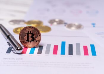 Un lapicero metálico y una moneda de bitcoin dorada parada de canto.