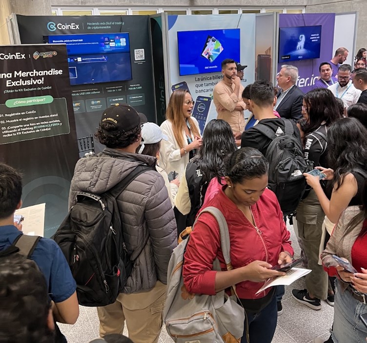 Un grupo numeroso de personas reunido frente al stand de CoinEx.
