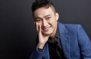 Justin Sun sonriendo delante de un fondo negro apoyando su mano en la cara.