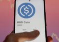 Una mano sosteniendo un teléfono en el que se ve el logo de USDC.
