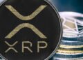 Una moneda física de XRP y detrás se observa otro puñado de monedas físicas apiladas unas sobre otras.