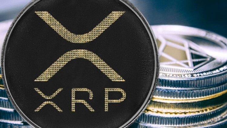 Una moneda física de XRP y detrás se observa otro puñado de monedas físicas apiladas unas sobre otras.