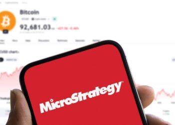Un móvil con el logo de Microstrategy y en el fondo el precio de bitcoin.