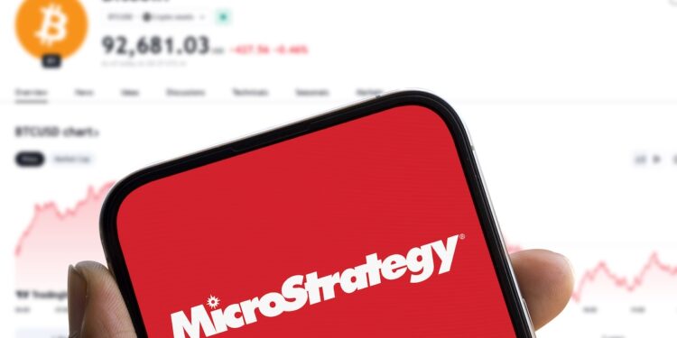 Un móvil con el logo de Microstrategy y en el fondo el precio de bitcoin.