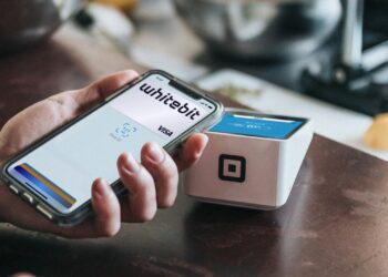Una mano varonil sostiene un teléfono celular con la app de WhiteBIT abierta cerca de de un punto de venta.