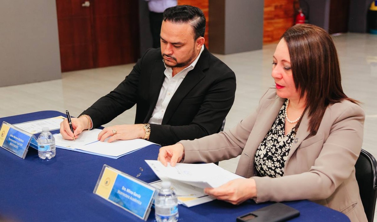 Un hombre sentado y en traje casual firma un documento al lado de una mujer.