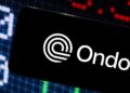 Logo de Ondo Finance en un smarphone con gráficas de precios en el fondo.