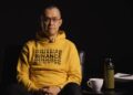 Changpeng Zhao (CZ), ex-CEO de Binance sentado luciendo un suéter amarillo con la palabra Binance repetida varias veces en el pecho.