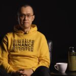 Changpeng Zhao (CZ), ex-CEO de Binance sentado luciendo un suéter amarillo con la palabra Binance repetida varias veces en el pecho.