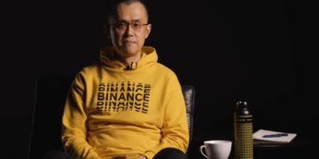 Changpeng Zhao (CZ), ex-CEO de Binance sentado luciendo un suéter amarillo con la palabra Binance repetida varias veces en el pecho.