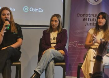 Tres mujeres con ropa casual sentadas conversan con el publico sobre un escenario.