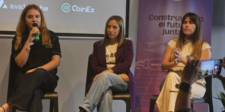 Tres mujeres con ropa casual sentadas conversan con el publico sobre un escenario.