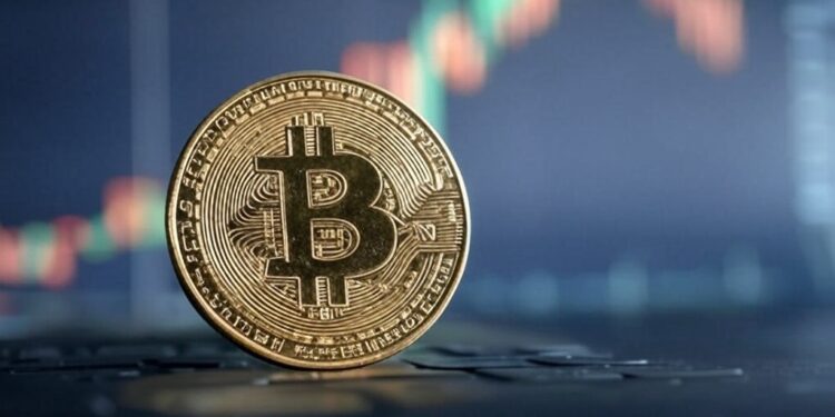 moneda de bitcoin sobre una mesa y de fondo un gráfico de precios.
