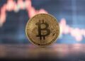 moneda de bitcoin sobre una mesa con un gráfico de precios en el fondo.