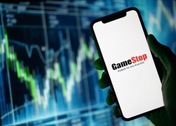 Gráfico de precio genérico de fondo, y una mano sosteniendo un teléfono con el logotipo de GameStop.
