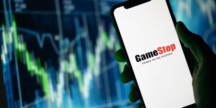 Gráfico de precio genérico de fondo, y una mano sosteniendo un teléfono con el logotipo de GameStop.