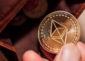 Una mano sosteniendo una moneda de ethereum cerca de una billetera