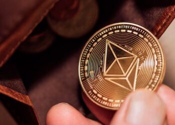 Una mano sosteniendo una moneda de ethereum cerca de una billetera