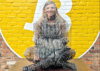 Una persona reflejada a través de la estatua de Satoshi Nakamoto en Tokio