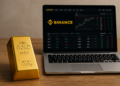 Lingote de oro al lado de una computadora. En el monitor se ve el logo de Binance.