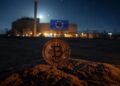 Una moneda de BTC junto a una bandera de la Unión Europea en una ciudad a oscuras.