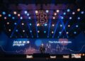 Imagen de un evento o conferencia en un auditorio con un escenario grande. En la pantalla principal del escenario aparece el logo de 'btc prague' y el texto 'The Future of Bitcoin'.