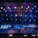Imagen de un evento o conferencia en un auditorio con un escenario grande. En la pantalla principal del escenario aparece el logo de 'btc prague' y el texto 'The Future of Bitcoin'.