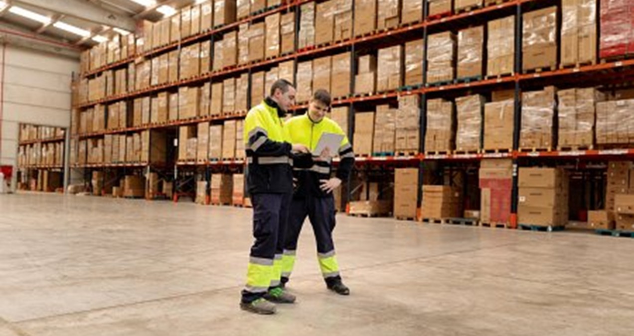 Dos trabajadores en bragas parados en un almacen de productos.