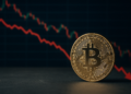 Moneda física de bitcoin y gráfico de precio cayendo.