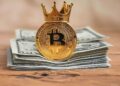 Una moneda de bitcoin con una corona y dólares debajo de ella.